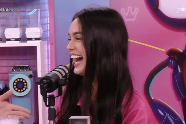 Larissa de camisa rosa, sorrindo, em frente a um microfone