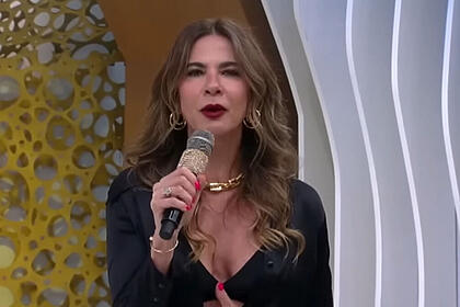 Luciana gimenez, em pé, no estúdio do superpop, com um microfone em mãos