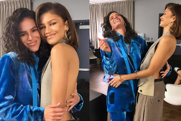 Bruna Marquezine de blazer e calça azul, sorrindo, abraçando Zendaya nos bastidores de evento