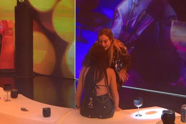 Bruna em pé de frente para Larissa que está sentada.