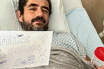 Felipe Andreoli deitado em uma cama de hospital, segundo uma folha escrito "Feliz Páscoa" e um potinho com as pedras retiradas do seu rim