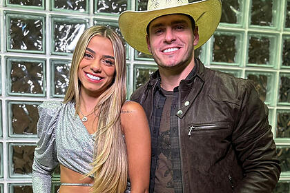 Key Alves sorrindo, com vestido cinza, cabelo solto, ao lado de Gustavo nos estúdios Globo
