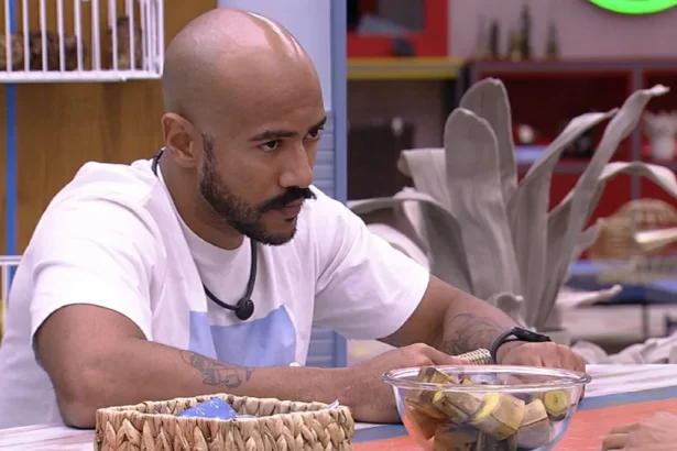 Ricardo de camisa branca, com semblante sério, com as mãos na mesa da cozinha do VIP do BBB 23