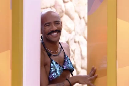 Ricardo sorrindo usando um biquini azul de Marvvila encostado na porta do Quarto Deserto