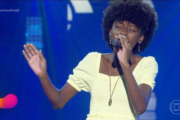 Alicia Rachel, de vestido bege, se apresenta na estreia do The Voice Kids 8