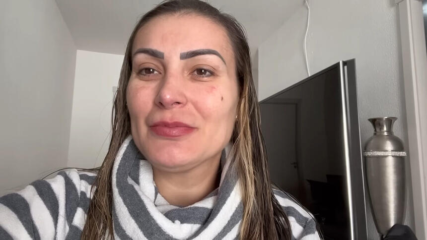Andressa Urach em trecho do seu vlog, na sala da sua casa, com uma televisão ao fundo