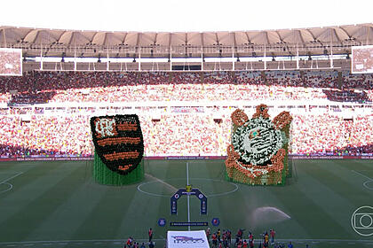 Trecho da transmissão da tv globo no jogo entre flamengo e corinthians, com os logos da equipe no gramado do maracanã