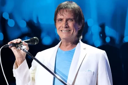 Roberto Carlos sorrindo, ce camisa azul e blazer branco, segurando um microfone