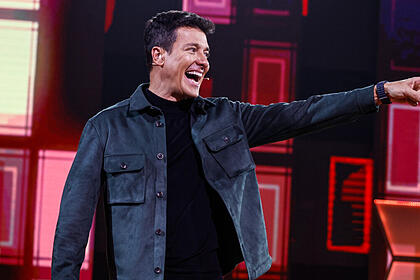 Rodrigo faro sorrindo e apontando para o lado no palco do canta comigo 5