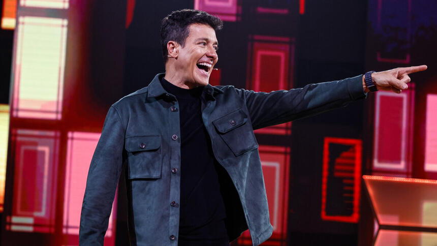 Rodrigo Faro sorrindo e apontando para o lado no palco do Canta Comigo 5