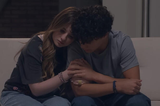 Sophia Valverde e Igor Jassen sentados, abraçados, em um sofá, em trecho da novela Poliana Moça