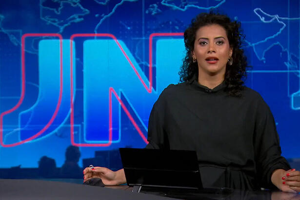 Aline Midlej com uma roupa preta na bancada do Jornal Nacional