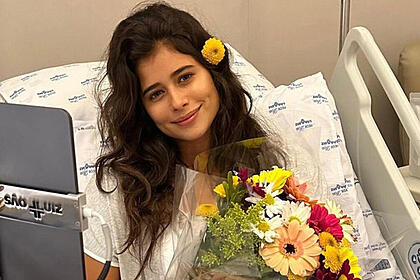 Isadora Cruz deitada em um leito de hospital com um flor por cima