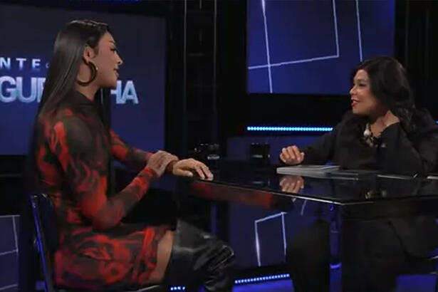 Pabllo Vittar de vestido, sentada, em frente a Blogueirinha
