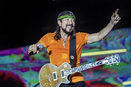Bell Maruqes sorrindo, de bandana, camisa laranja, guitarra presa no pescoço, em cima do trio elétrico durante micareta