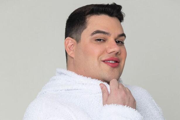Erick Ricarte sorrindo, de camisa branca, com a mão no queixa