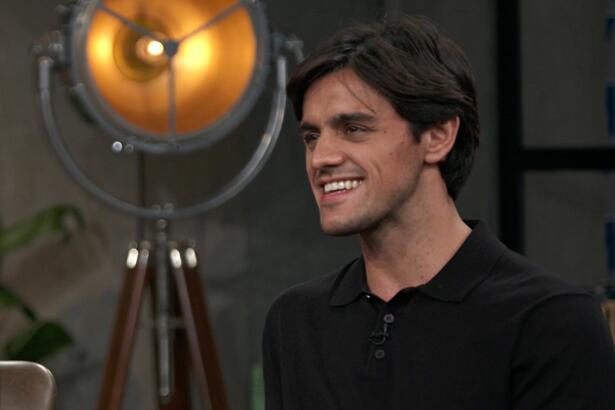 Felipe Simas sorrindo, de camisa preta, sentado em frente a Pedro Bial durante entrevista