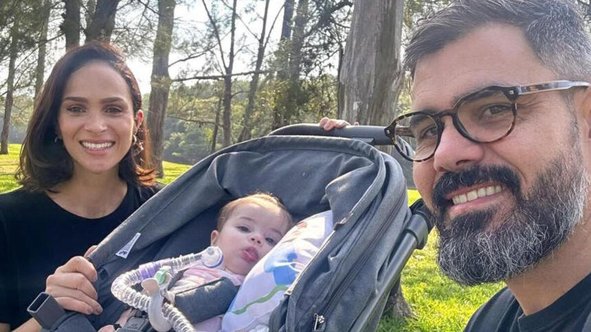 Juliano Cazarré e Leticia Cazarré em foto posada ao lado da filha, no carrinho e com o tubo de traqueostomia