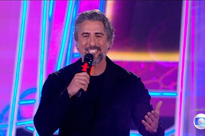 Marcos Mion sorrindo, de camisa preta, no palco do Criança Esperança