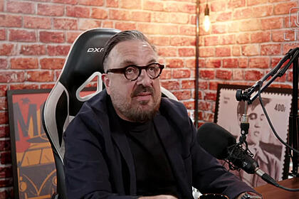 Rodrigo Carelli de camisa manga longa preta, sentado numa cadeira de gamer, de oculos de grau