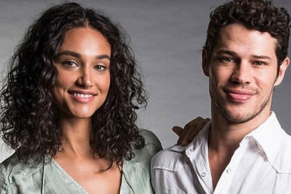 Debora Nascimento de camisa cinza, sorrindo, de cabelo solto, ao lado de José Loreto, sorrindo, de camisa branca, durante ensaio fotográfico para a TV Globo