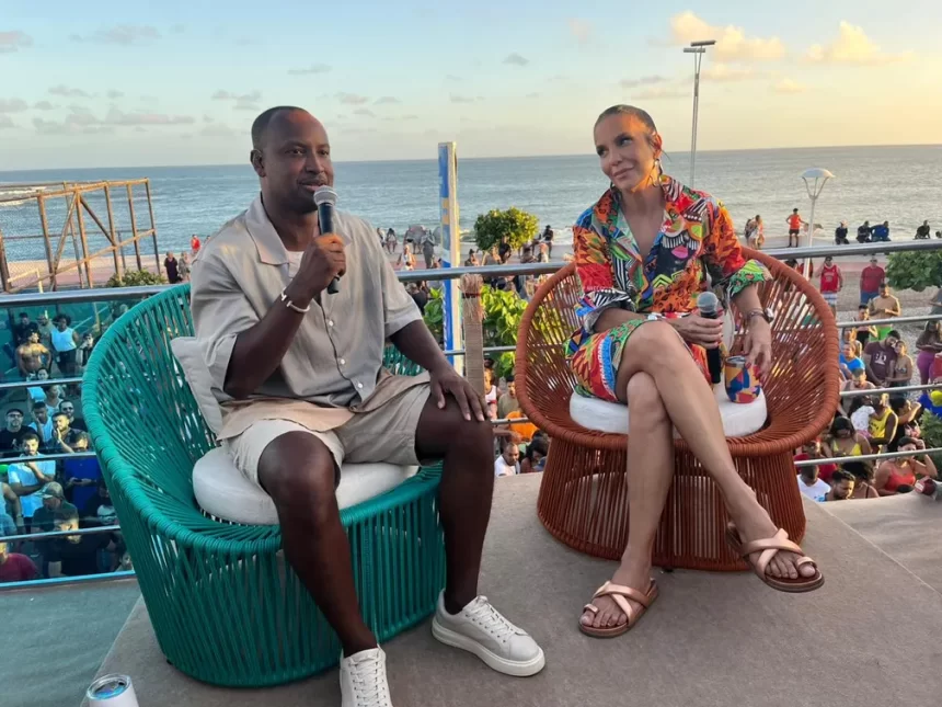 Ivete Sangalo sentada no banco ao lado de Thiaguinho, em cima de um trio elétrico durante gravação do Pipoca da Ivete