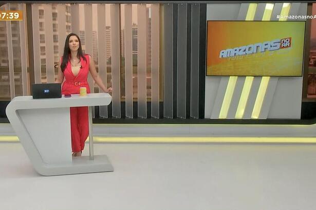 Cenário do Amazonas no AR com Larissa Santiago no centro em pé, vestindo macacão vermelho