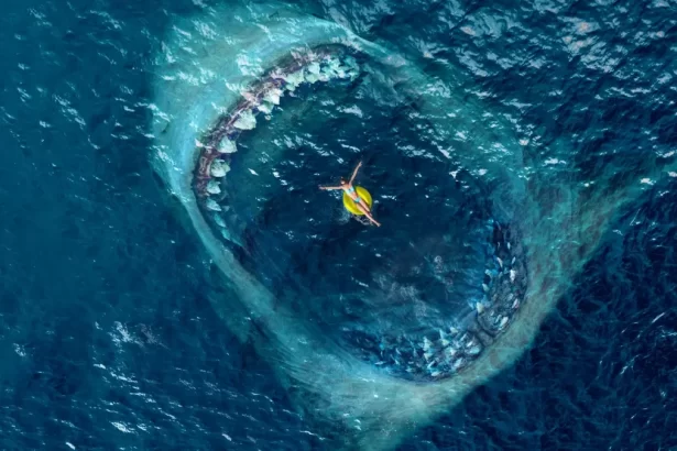 Pessoa em boia amarela e verde no oceano, cercada pela boca gigante de um megatubarão; cena de suspense e perigo do filme Megatubarão