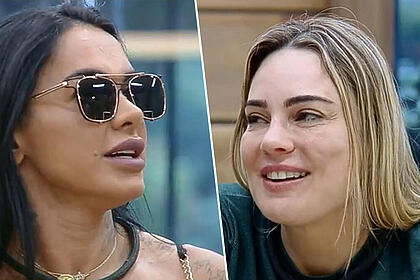 Simioni de óculos escuro e Rachel Sheherazade na cozinha de A Fazenda, ambas estão sorrindo