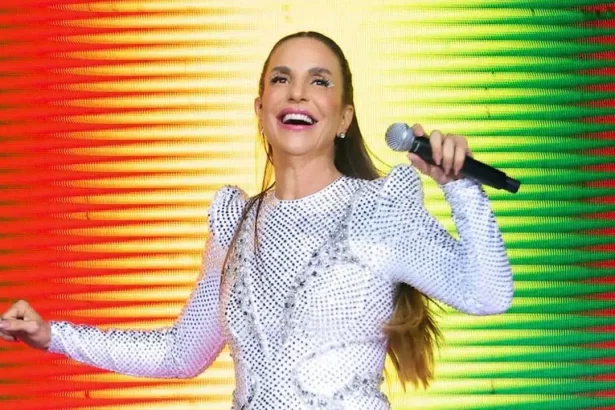 Ivete Sangalo de look branco, com os braços abertos, segurando um microfone, durante show