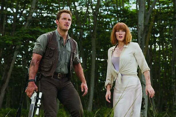 Homem com arma na mão ao lado de uma mulher assustada em cena do filme Jurassic World: O Mundo Dos Dinossauros