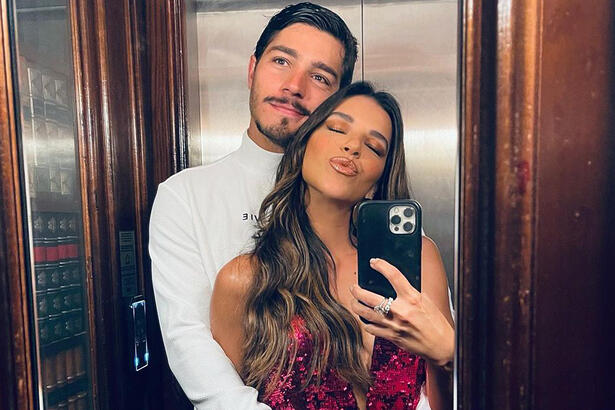 Mariana Rios de cabelo solto, soltando beijo, segurando o celular, abraçada com o namorado no elevador