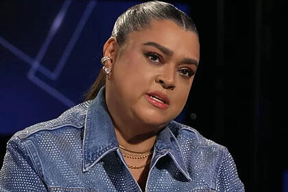 Preta Gil de jaqueta jeans, com a cabeça virada pro lado esquerdo, sentada durante entrevista
