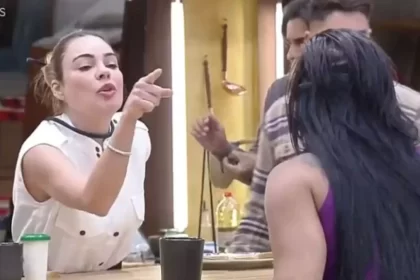 Rachel Sheherazade de camisa branca, microfone no pescoço apontando o dedo para Jenny na cozinha durante dinâmica