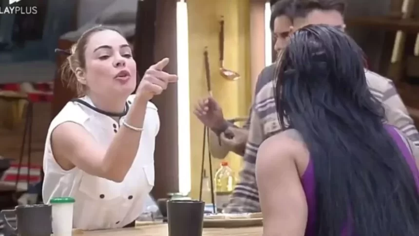 Rachel Sheherazade de camisa branca, microfone no pescoço apontando o dedo para Jenny na cozinha durante dinâmica