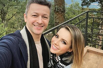 Sandy com cabelo solto, curto, sorrindo, usando cachecol, abraçada com Lucas Lima durante viagem