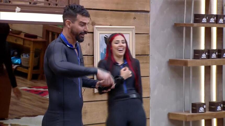 Alicia X sorrindo na sala de A Fazenda 15, enquanto Radamés explica Prova de Fogo
