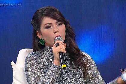 Nadja durante Hora do Faro, segurando microfone, vestida com uma roupa prateada.