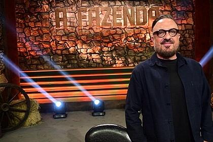 Rodrigo Carelli de paleto, camisa social e grava pretos, com a mão no bolso, sorrindo, com oculos de grau