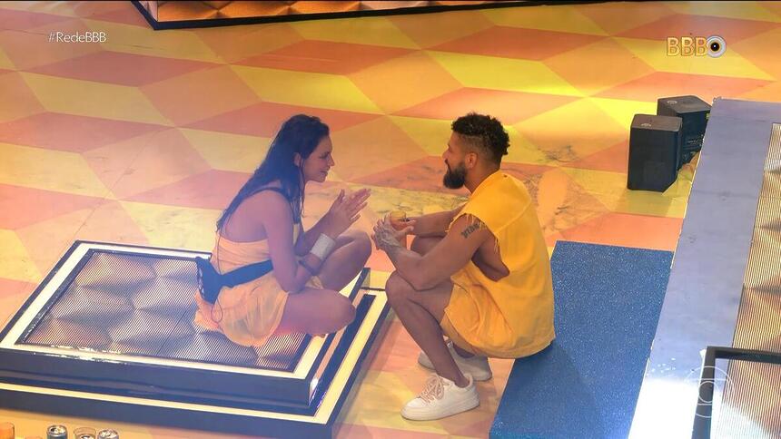 Juninho conversa com Alane, acocorados no chão do palco da festa do BBB 24