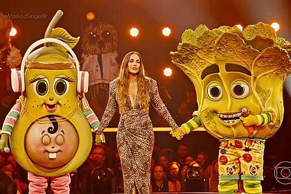 Ivete Sangalo segura a mão da Mamãe Abacate e Pé de Alface no cenário do The Masked Singer Brasil 4