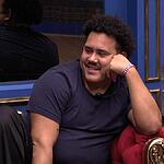 Lucas com a mão no queixo, sentado no sofá da sala e sorrindo, após a Prova do Líder do BBB 24