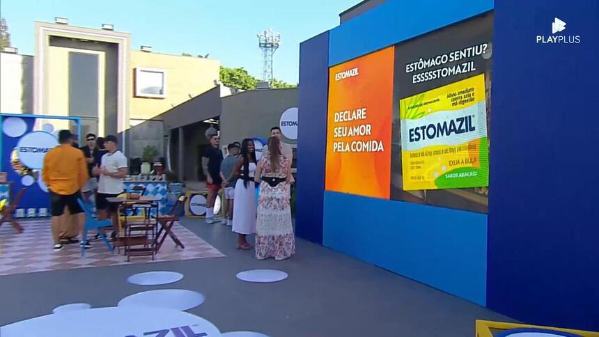 Cenário da atividade patrocinada pelo Estomazil na área externa da Mansão do A Grande Conquista contendo mesinhas, pastel, hambúrguer e muito mais