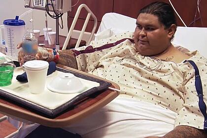 Michael sentado na cama de hospital comendo em cena de quilos mortais