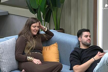 Dona Geni com a mão na cabeça no sofá do A Grande Conquista 2