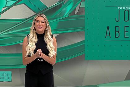 Renata Fan com as mãos unidas, sorrindo, no cenário do Jogo Aberto