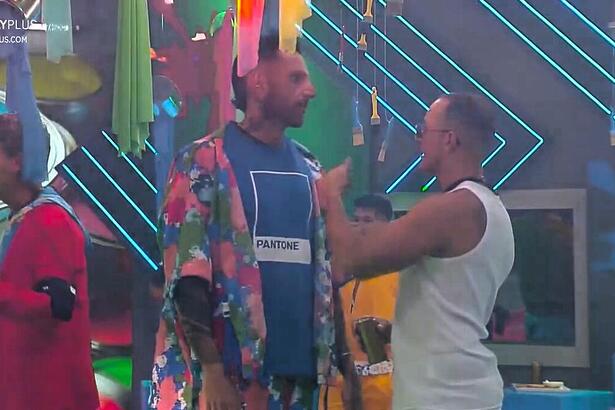 Guipa olha para Fellipe no centro do palco da Festa das Cores, eles falam de Dona Geni no A Grande Conquista