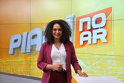 Thracy oliveira sorrindo em frente o telão com o logo do piauí no ar, que carrega tons amarelo e laranja, padrão da record