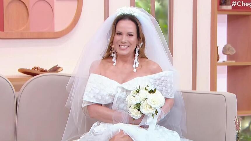 Regina Volpato vestida de noiva e sentada no sofá do Chega Mais