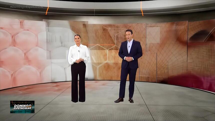 Carolina Ferraz e Eduardo Ribeiro sorrindo em pé no cenário do Domingo Espetacular